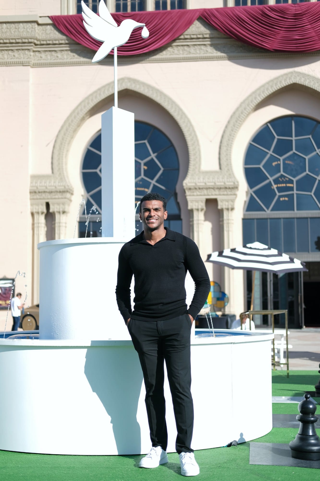 An attendee in black smiling in front of the summit fountain and its white bird sculpture