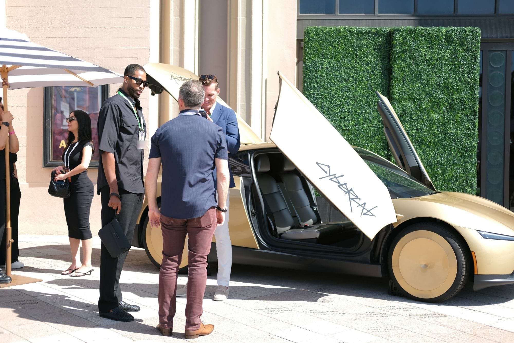 A small group talking beside a gold concept car, one of them holding up a phone