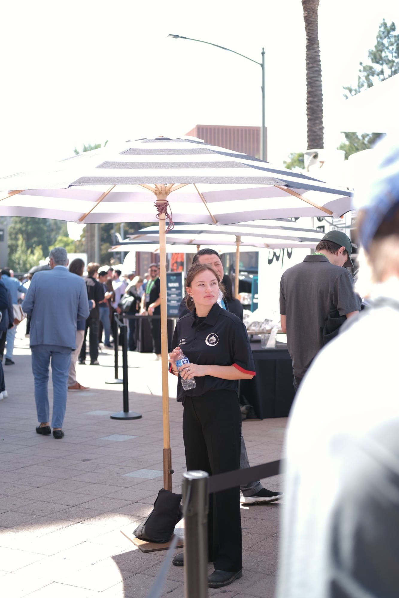 A guest services staff member holding a water bottle under a striped umbrella