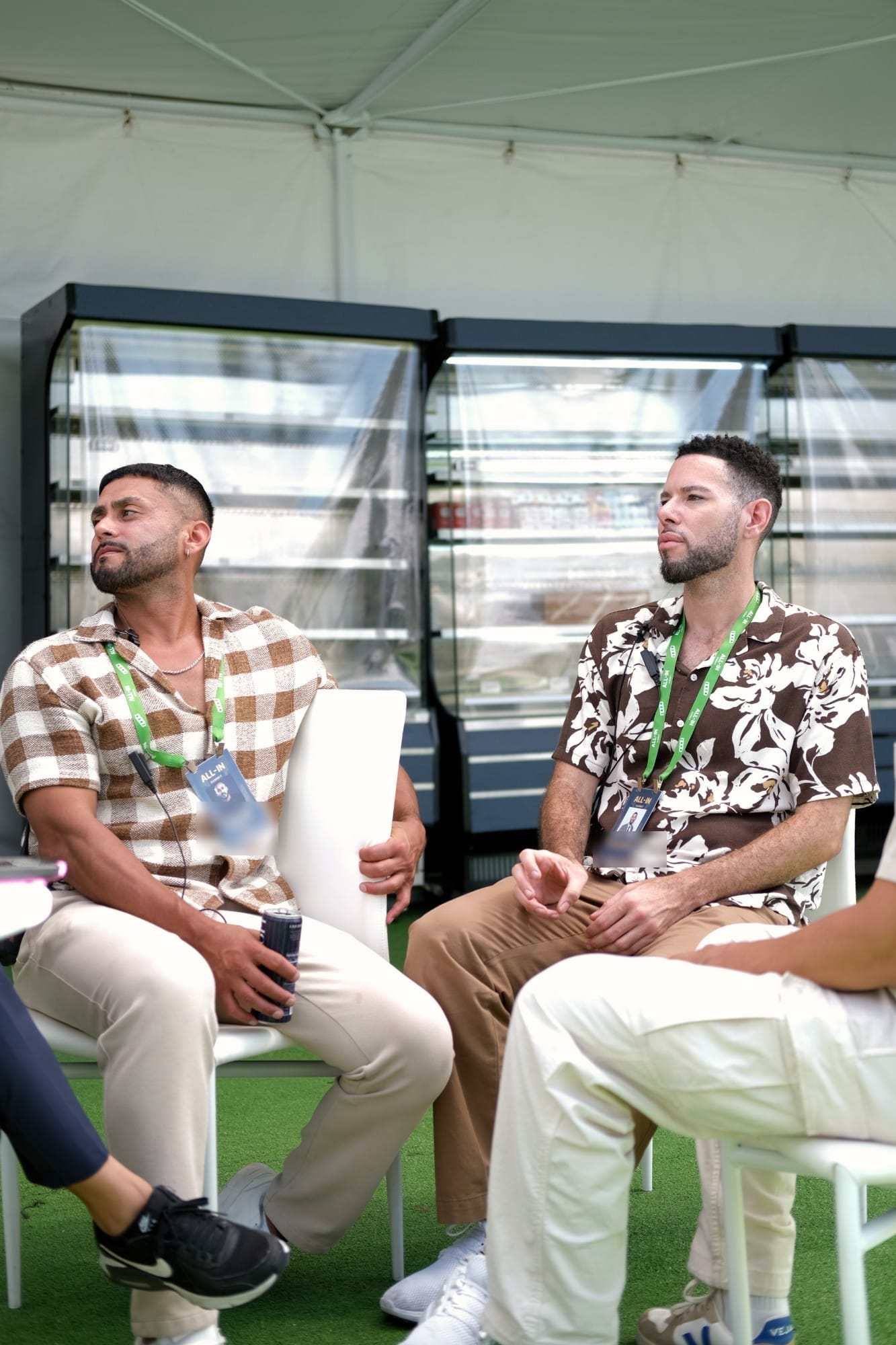 Two attendees in patterned shirts listening during a small group discussion in a tent